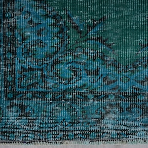 May include: Close-up of a teal blue rug with a faded floral pattern. The rug has a distressed look and a fringe border.