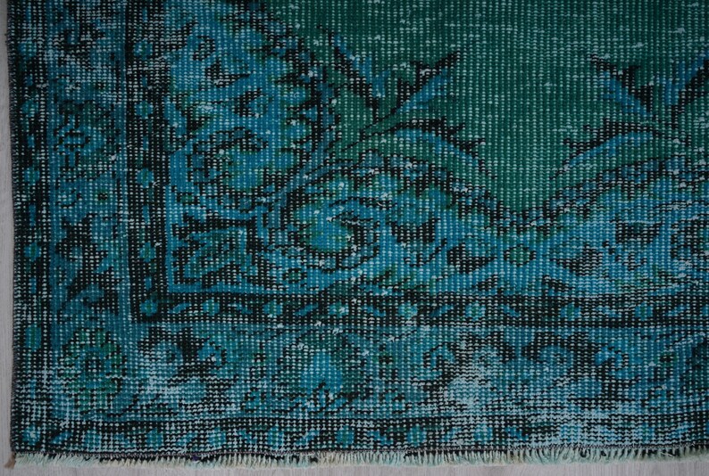 May include: Close-up of a teal blue rug with a faded floral pattern. The rug has a distressed look and a fringe border.