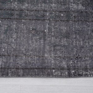 May include: Close-up of a distressed gray rug with a textured, woven pattern. The rug features horizontal stripes and a faded appearance, suggesting a vintage or antique style. The rug's color palette is primarily gray and white.
