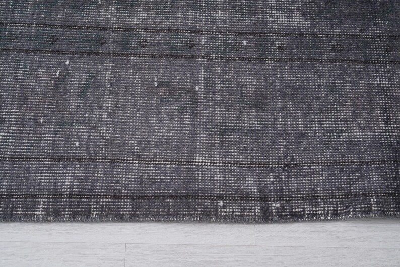 May include: Close-up of a distressed gray rug with a textured, woven pattern. The rug features horizontal stripes and a faded appearance, suggesting a vintage or antique style. The rug's color palette is primarily gray and white.