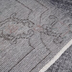 May include: Close-up of a gray and white patterned rug with a distressed design. The rug has a textured surface with a geometric pattern and a white fringe along the edge. The rug is folded over.