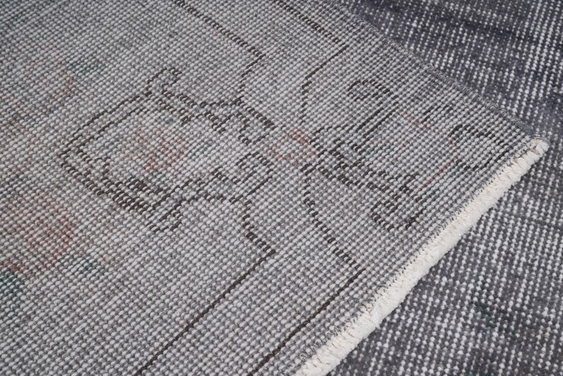 May include: Close-up of a gray and white patterned rug with a distressed design. The rug has a textured surface with a geometric pattern and a white fringe along the edge. The rug is folded over.