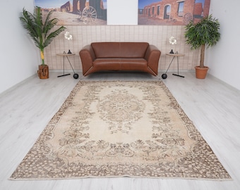 May include: A vintage cream-colored rug with a brown floral pattern. The rug has a distressed look and is laid out on a light wood floor.