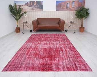 Könnte beinhalten: Ein roter Vintage-Teppich mit einem verblassten weißen Muster. Der Teppich liegt auf einem hellen Holzboden in einem Raum mit einem braunen Ledersofa und zwei Beistelltischen.