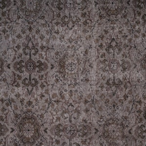 May include: A close-up of a brown and grey patterned rug with a distressed look. The rug has a floral design and a subtle sheen.
