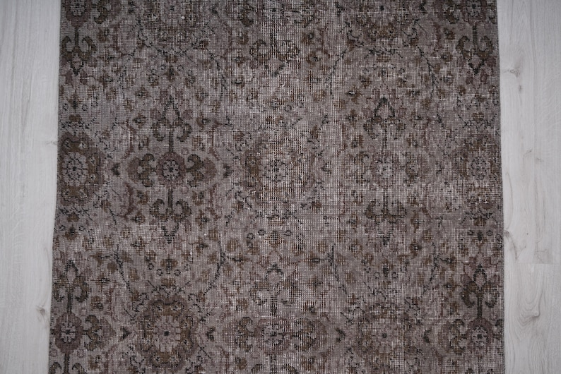 May include: A close-up of a brown and grey patterned rug with a distressed look. The rug has a floral design and a subtle sheen.