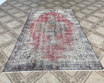 May include: A vintage rug with a faded red center and a floral pattern. The rug has a distressed look with a worn and faded appearance. The rug is rectangular and has a fringe border.
