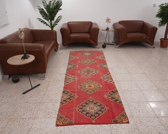 May include: A red, patterned rug with a geometric design. The rug is laid out on a white tiled floor in a room with brown leather chairs.