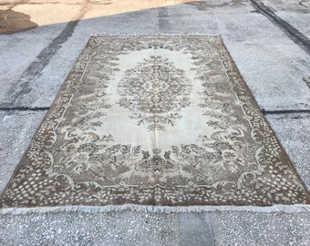 May include: A vintage rug with a cream background and a brown floral pattern. The rug has a fringe border.