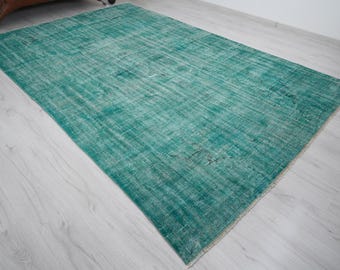 May include: A rectangular, distressed-look rug in shades of teal and white. The rug has a faded appearance with a textured surface. The rug is placed on a light-colored wooden floor, showcasing its color and design.