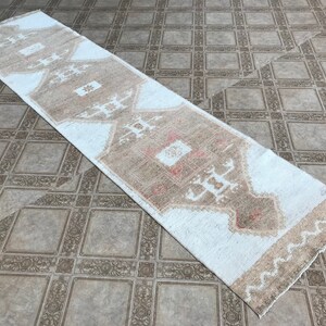 May include: A white runner rug with a brown and beige geometric pattern. The rug has a fringed edge.