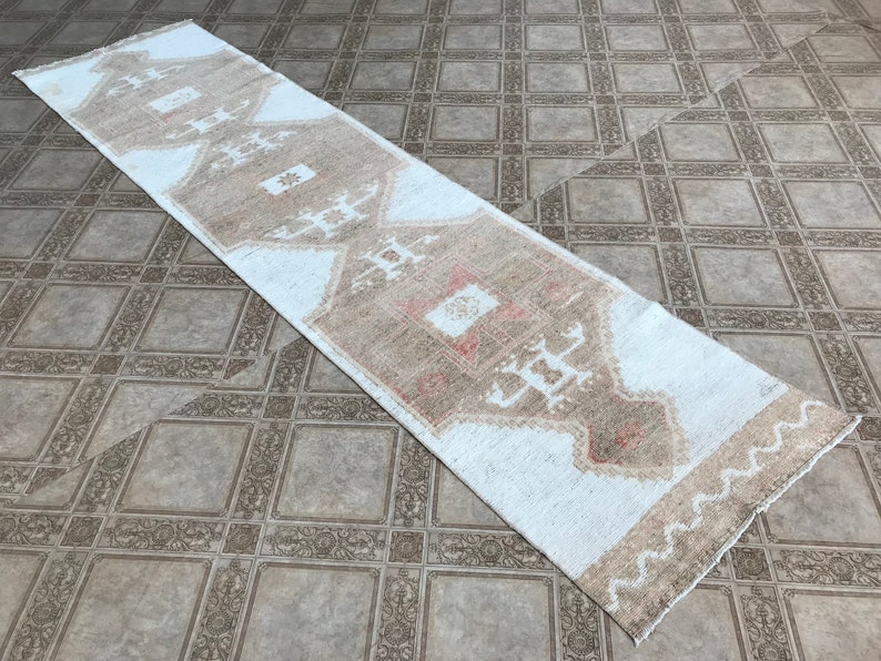 May include: A white runner rug with a brown and beige geometric pattern. The rug has a fringed edge.