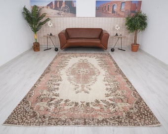 May include: A vintage cream-colored rug with a brown and pink floral pattern. The rug has a distressed look and is perfect for adding a touch of bohemian style to any room.