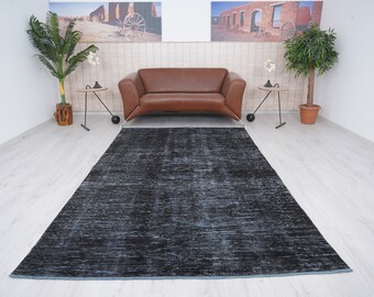 May include: A dark blue distressed rug with a subtle pattern. The rug is laid out on a light wood floor in a room with a brown leather sofa and two side tables.