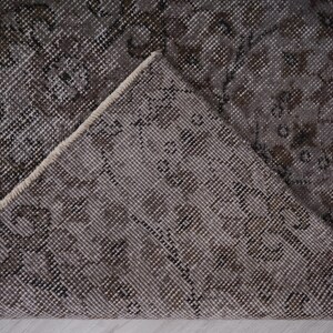 May include: Close-up of a grey and white patterned rug with a floral design. The rug is folded in half, showing the underside of the fabric.