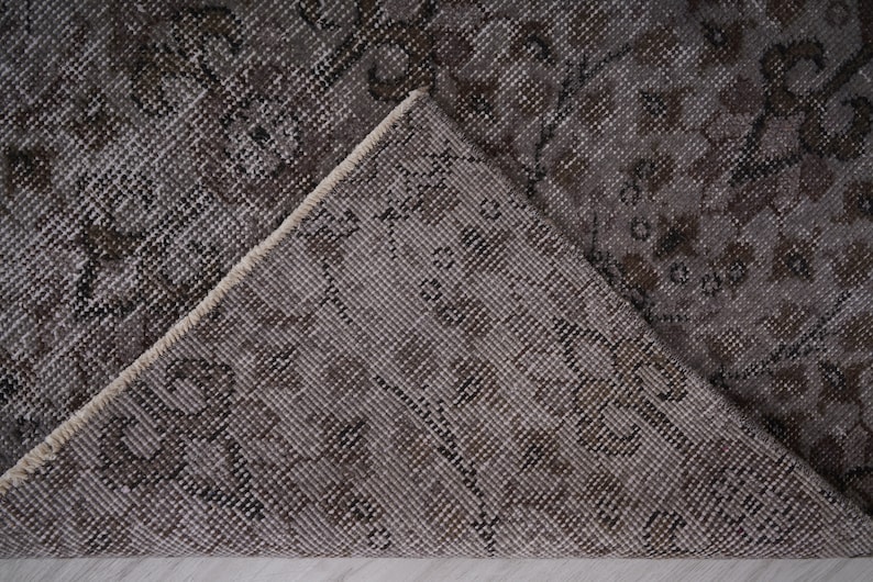 May include: Close-up of a grey and white patterned rug with a floral design. The rug is folded in half, showing the underside of the fabric.