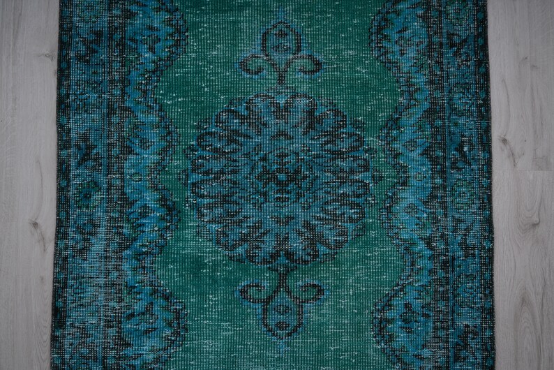 May include: A vintage teal and blue rug with a floral pattern. The rug has a distressed look and is made of a soft, woven material.