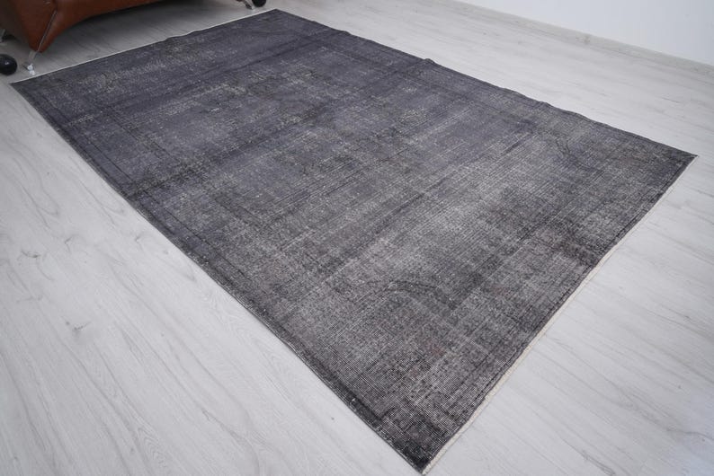 May include: A rectangular, distressed-look rug in shades of gray and black. The rug has a faded appearance with visible texture and a subtle pattern. The rug is placed on a light-colored wooden floor.