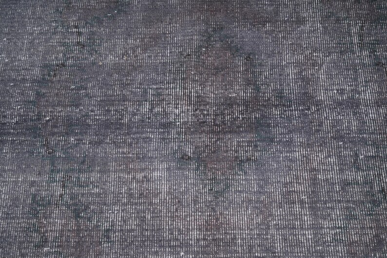 May include: A close-up of a distressed, dark gray rug with a textured surface. The rug has a vertical striped pattern with lighter gray and white accents, creating a vintage or antique appearance.