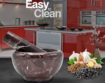 May include: A red marble mortar and pestle set on a gray countertop. The mortar and pestle are made of red marble with white veins. The mortar is round and has a wide base. The pestle is long and has a rounded end. The mortar and pestle are surrounded by various spices, including garlic, ginger, and black peppercorns. The text "Easy to Clean" and "Detergent Safe" are visible in the image. The text "Perfect for all your grinding needs" is also visible in the image.
