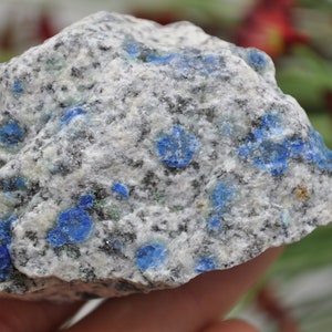 May include: A close-up of a rough, gray rock with blue and green flecks. The rock is speckled with small, blue crystals.
