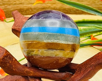 May include: A seven chakra crystal sphere on a wooden stand. The sphere is made of amethyst, clear quartz, green aventurine, yellow citrine, orange carnelian, red jasper, and a blue lapis lazuli band.