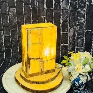 May include: A yellow onyx lamp with a wooden base on a white marble plate. The lamp is lit and casting a warm glow. The lamp is on a wooden base with three tiers.