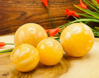 May include: Four smooth, polished orange calcite spheres of varying sizes on a wooden surface. The spheres are arranged in a cluster, with the largest sphere in the centre.