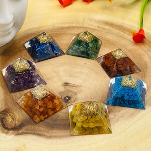 May include: Seven chakra crystal pyramids, each with a different color and type of crystal, arranged in a circle on a wooden surface. The crystals are amethyst, clear quartz, citrine, carnelian, green aventurine, lapis lazuli, and red jasper.