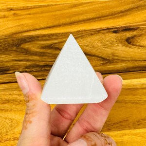 Puede incluir: Un cristal de pir&aacute;mide de selenita blanca, un tipo de mineral conocido por sus propiedades calmantes y purificadoras.