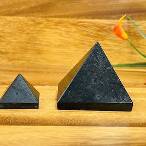May include: Two black obsidian pyramids, one larger than the other, on a wooden surface. The larger pyramid is about 2 inches tall and the smaller pyramid is about 1 inch tall.