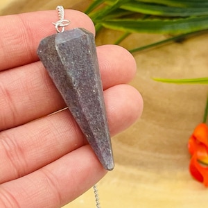May include: A purple amethyst crystal pendulum on a silver chain. The pendulum is pointed and has a faceted shape.