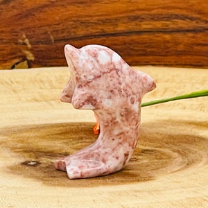 Puede incluir: Una figurita de delf&iacute;n de m&aacute;rmol rosa y blanco. El delf&iacute;n est&aacute; tallado en una pose de salto con la cola enroscada.