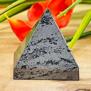 May include: Black obsidian pyramid crystal, a dark, geometric shape with a smooth, polished surface.