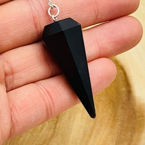 May include: Black obsidian pendulum with a silver chain. The pendulum is shaped like a point and has a faceted design.