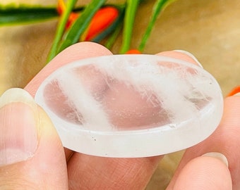 May include: A white oval-shaped selenite crystal with striations. The crystal is smooth and polished.