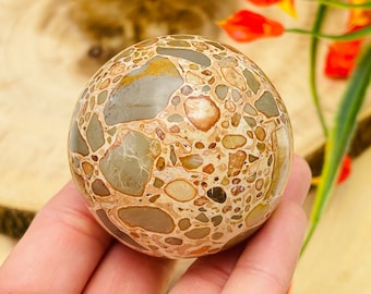 May include: A smooth, round, beige, brown, and grey bumblebee jasper sphere. The sphere has a mottled, speckled, and marbled pattern.