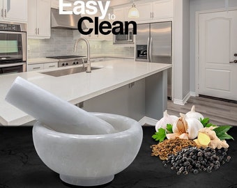 May include: White marble mortar and pestle set on a black surface. The mortar and pestle are made of white marble and have a smooth, polished finish. The set is perfect for grinding spices, herbs, and other ingredients. "DETERGENT SAFE" and "PERFECT FOR ALL YOUR GRINDING NEEDS" are printed in black text on the surface.