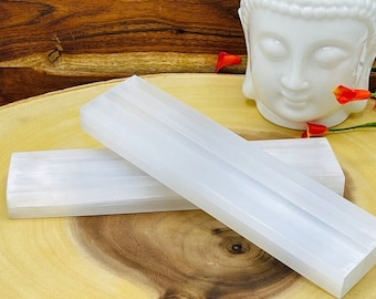May include: Two white selenite charging plates on a wooden surface. The plates are smooth and have a natural, striated texture.