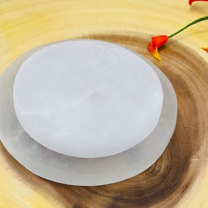 May include: Two white selenite charging plates, one on top of the other, on a wooden surface. The plates are smooth and have a natural, slightly cloudy appearance.