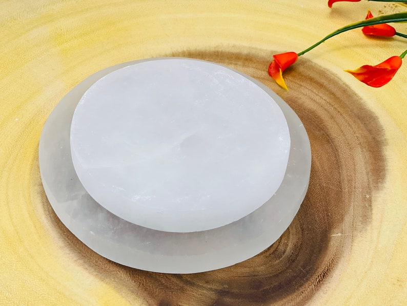 May include: Two white selenite charging plates, one on top of the other, on a wooden surface. The plates are smooth and have a natural, slightly cloudy appearance.