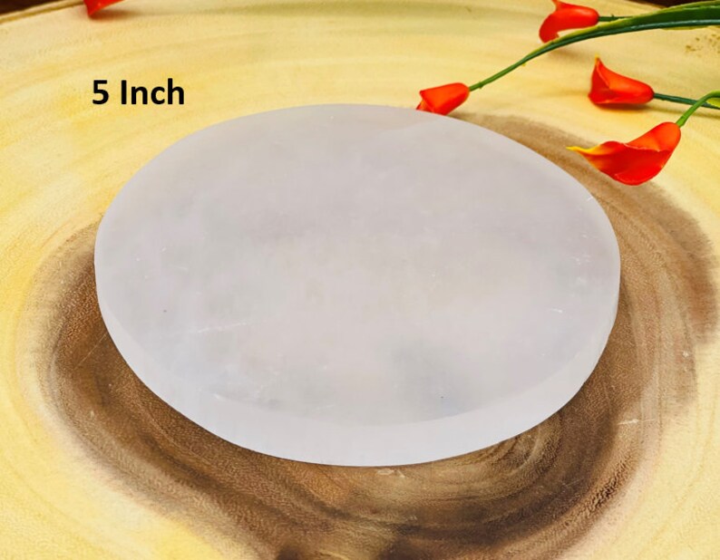 May include: A 5 inch white selenite charging plate, a smooth, round, white disc on a wooden surface.