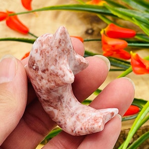 Puede incluir: Una peque&ntilde;a figura de delf&iacute;n tallada a mano en m&aacute;rmol rosa y marr&oacute;n. El delf&iacute;n est&aacute; en una pose juguetona, con la cola levantada y la cabeza echada hacia atr&aacute;s.