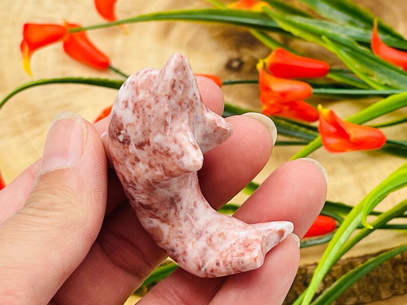 Puede incluir: Una peque&ntilde;a figura de delf&iacute;n tallada a mano en m&aacute;rmol rosa y marr&oacute;n. El delf&iacute;n est&aacute; en una pose juguetona, con la cola levantada y la cabeza echada hacia atr&aacute;s.