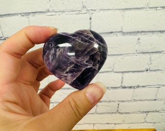 May include: A heart-shaped amethyst crystal with a deep purple color and a swirling pattern. The crystal is polished and smooth.