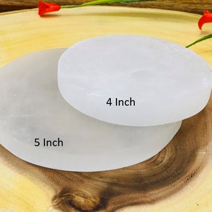 May include: Two white selenite charging plates, one 4 inches in diameter and the other 5 inches in diameter, on a wooden surface.