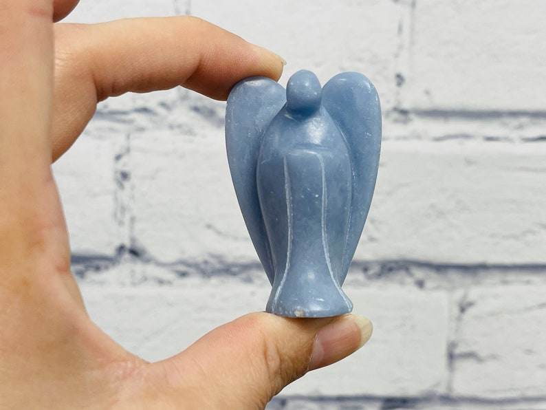 May include: A small, light blue angel figurine carved from a single piece of stone. The angel has wings and a simple, elegant design.