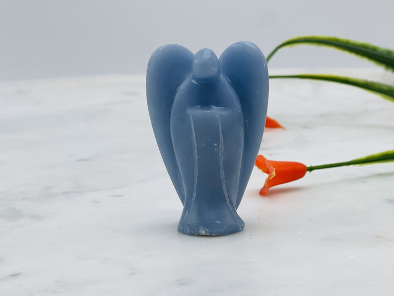 May include: A light blue angel figurine carved from selenite crystal. The angel has wings and a long flowing robe.