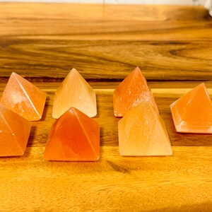 May include: Seven small orange and white crystal pyramids arranged in a row on a wooden surface.