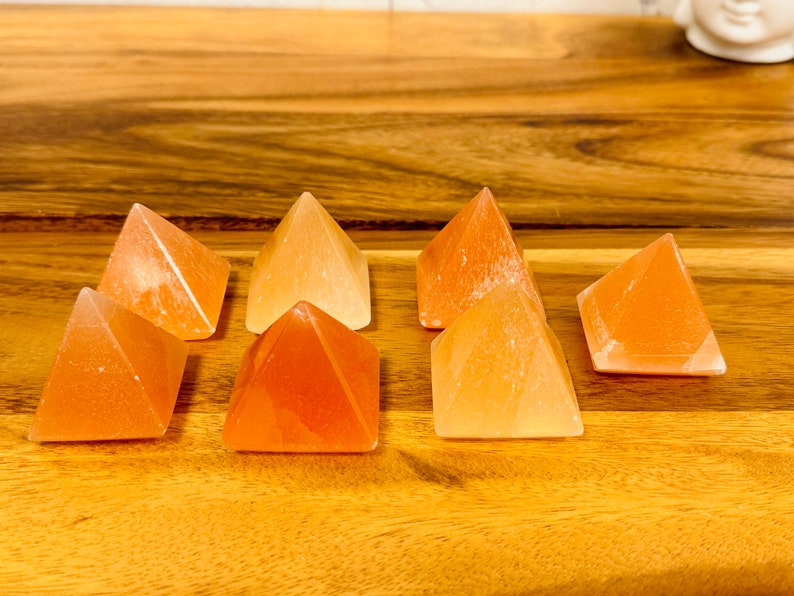 May include: Seven small orange and white crystal pyramids arranged in a row on a wooden surface.
